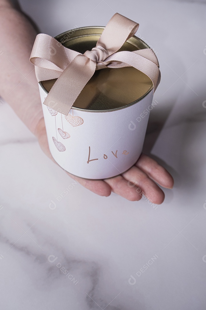 Uma caixa branca circular com uma tampa de metal sobre a mão de uma mulher