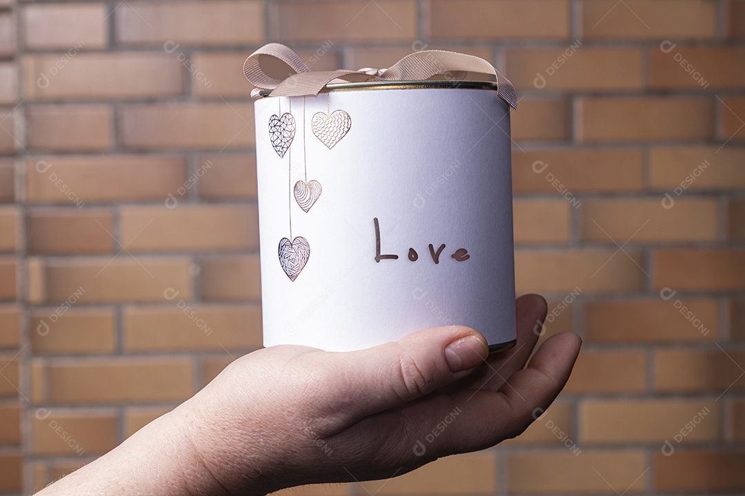 Uma caixa branca circular com uma tampa de metal sobre a mão de uma mulher