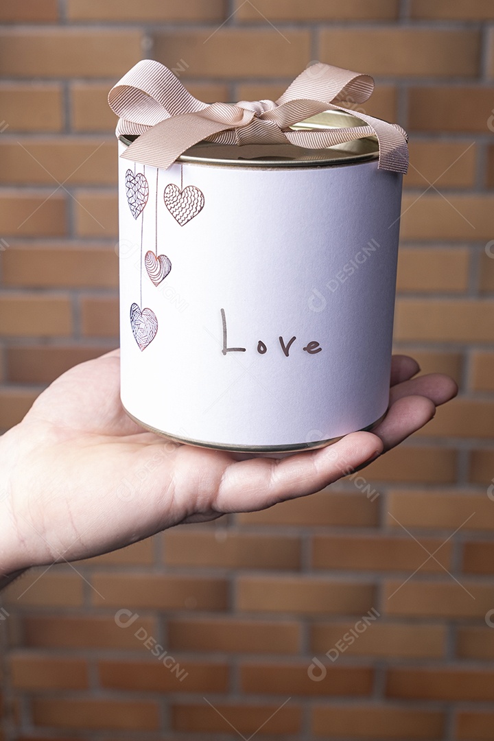 Uma caixa branca circular com uma tampa de metal sobre a mão de uma mulher