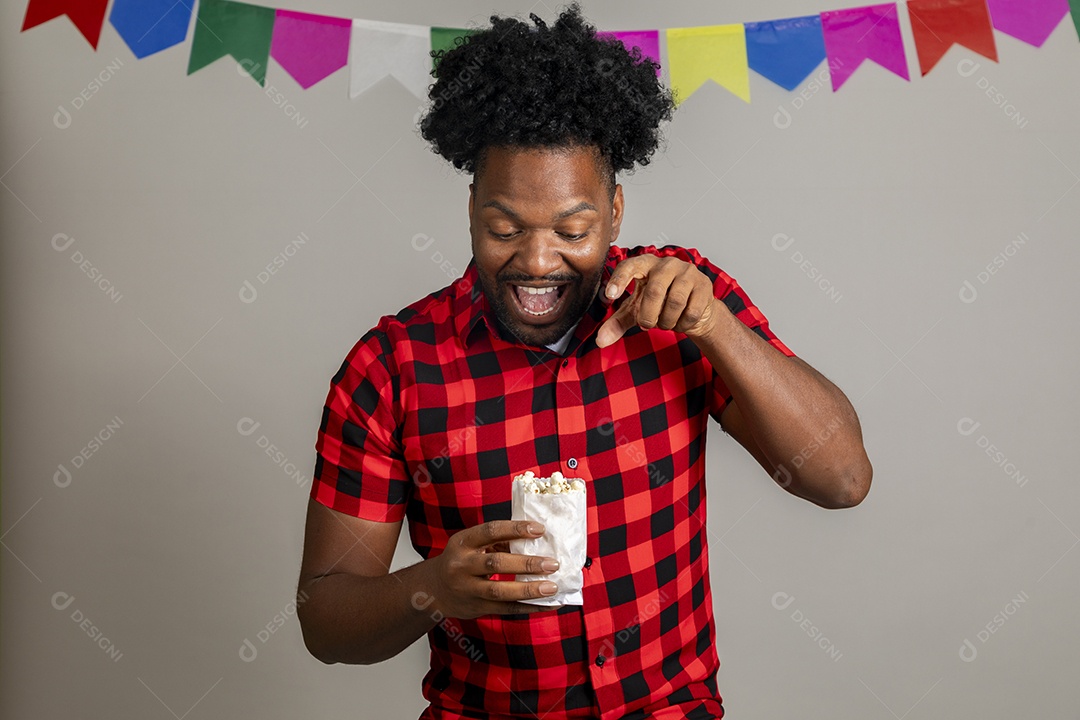 Homem jovem usando roupas típicas festa junina sobre fundo isolado se alimentando