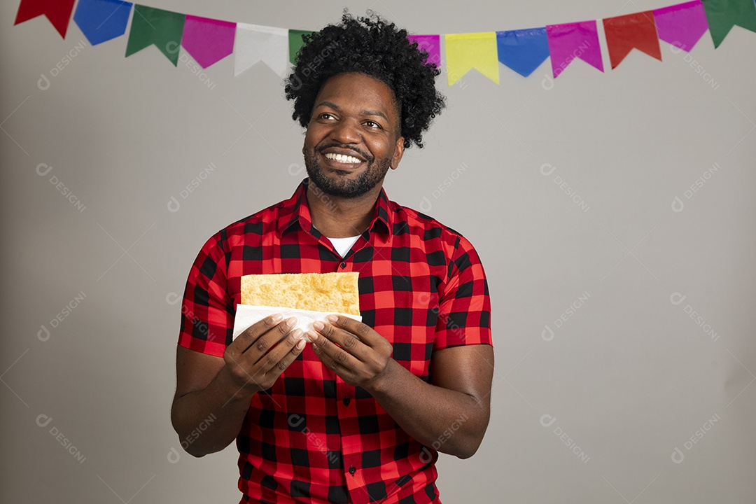Homem jovem usando roupas típicas festa junina sobre fundo isolado se alimentando