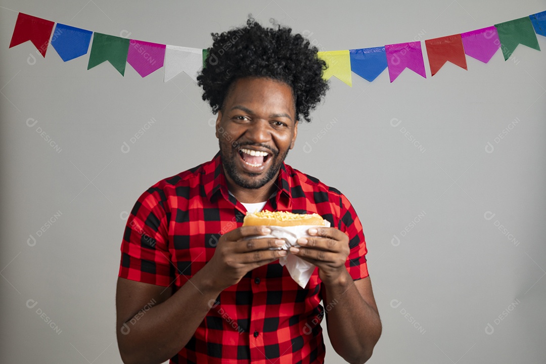 Homem jovem usando roupas típicas festa junina sobre fundo isolado se alimentando