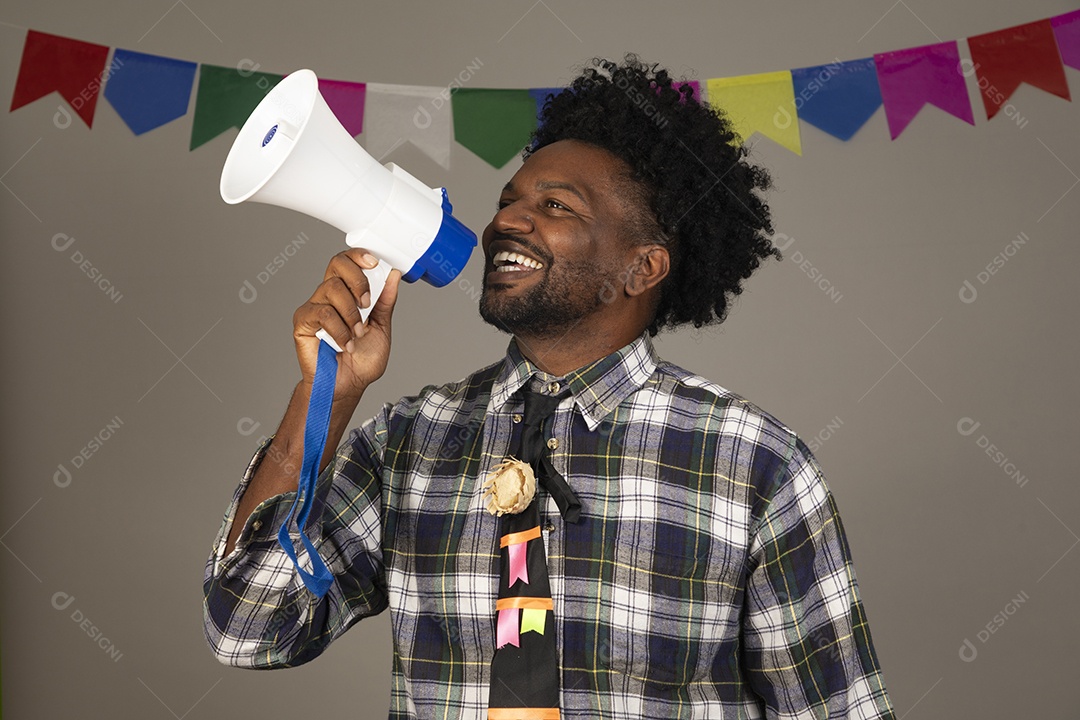 Homem jovem negro usando roupas típicas festa junina sobre fundo isolado usando megafone