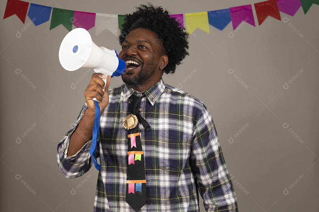 Homem jovem negro usando roupas típicas festa junina sobre fundo isolado usando megafone