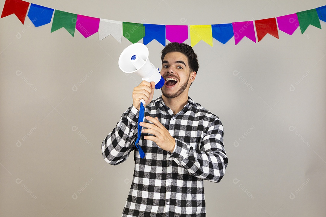 Homem jovem usando roupas típicas festa junina sobre fundo isolado segurando megafone