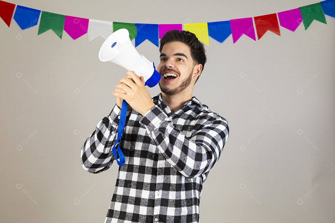 Homem jovem usando roupas típicas festa junina sobre fundo isolado segurando megafone