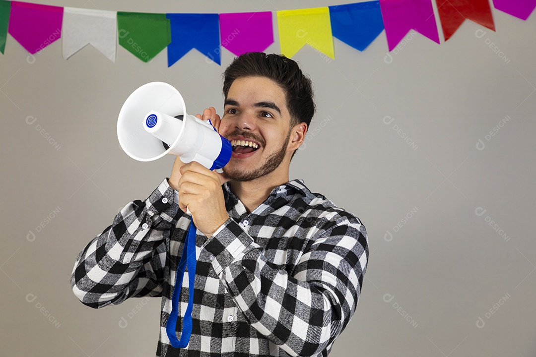 Homem jovem usando roupas típicas festa junina sobre fundo isolado segurando megafone