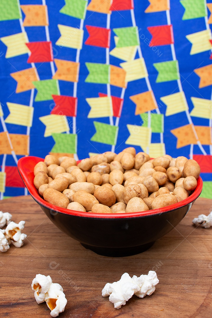 A imagem mostra uma tigela cheia de amendoim torrado e alguns grãos de pipoca espalhados sobre uma superfície de madeira