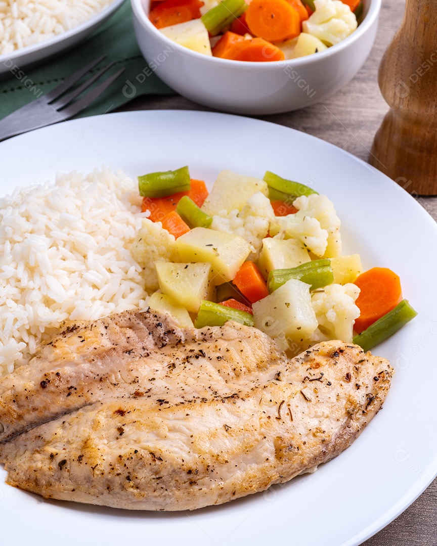 Imagem mostra um prato de filé de frango grelhado acompanhado por arroz branco e um mix de legumes