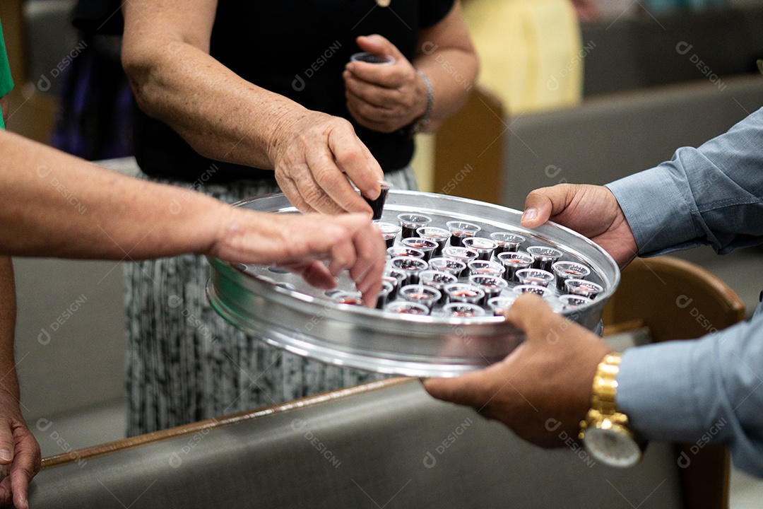 Mão de uma mulher pegando santa ceia em uma bandeija sob uma igreja