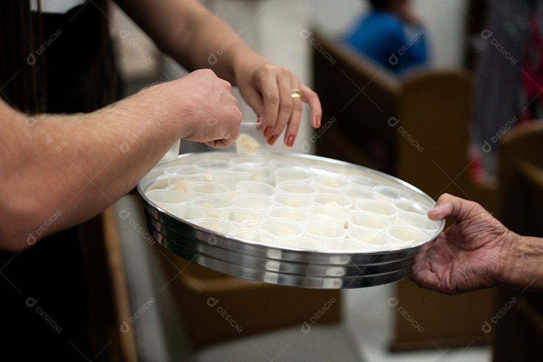 Mão de uma mulher pegando santa ceia em uma bandeija sob uma igreja