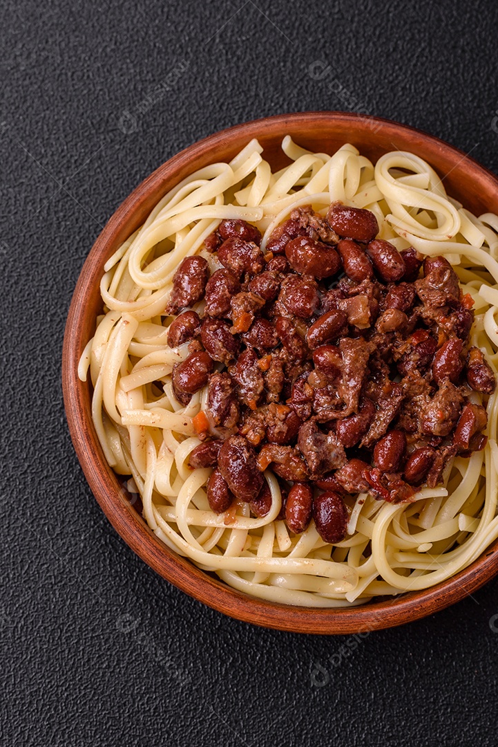 Macarrão de arroz com feijão, carne, molho de tomate, especiarias e ervas em um fundo de concreto escuro
