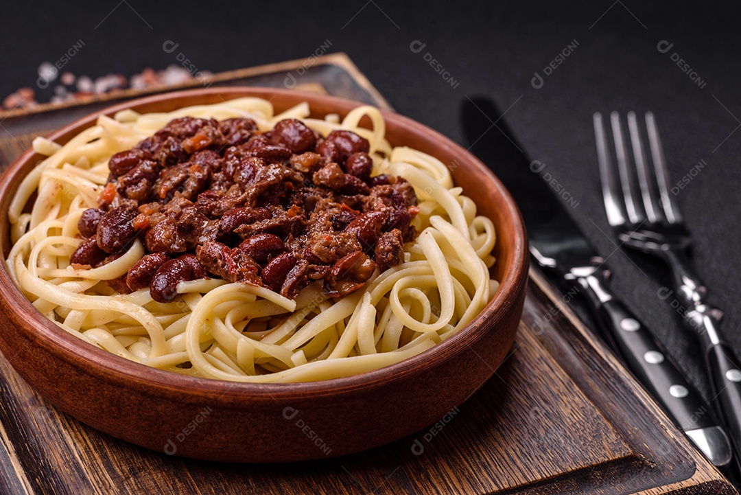 Macarrão de arroz com feijão, carne, molho de tomate, especiarias e ervas em um fundo de concreto escuro