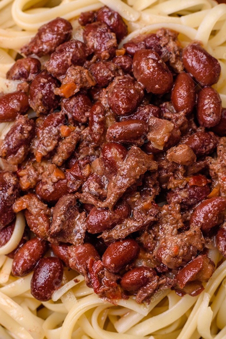 Macarrão de arroz com feijão, carne, molho de tomate, especiarias e ervas em um fundo de concreto escuro