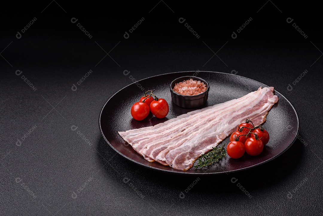 Imagem mostra fatias de bacon cru, acompanhadas de tomates cereja e sal rosa.