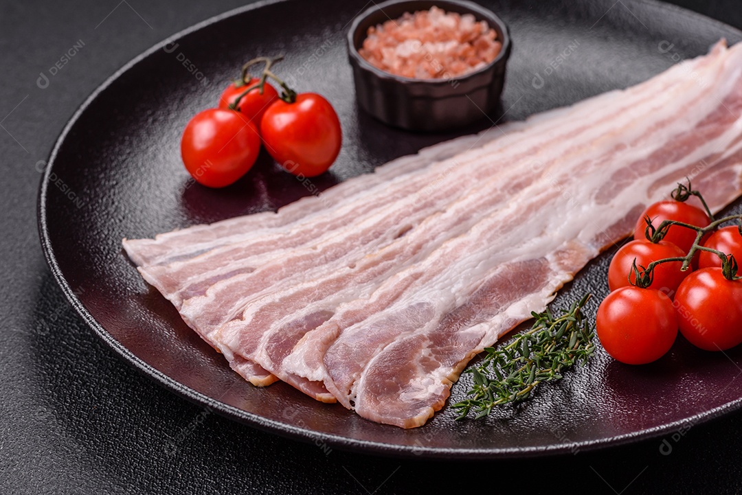 Imagem mostra fatias de bacon cru, acompanhadas de tomates cereja e sal rosa.