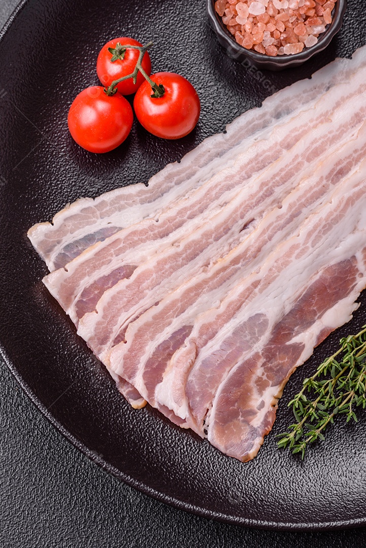 Imagem mostra fatias de bacon cru, acompanhadas de tomates cereja e sal rosa.