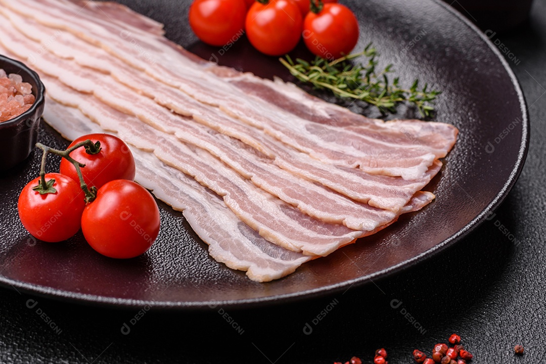 Imagem mostra fatias de bacon cru, acompanhadas de tomates cereja e sal rosa.