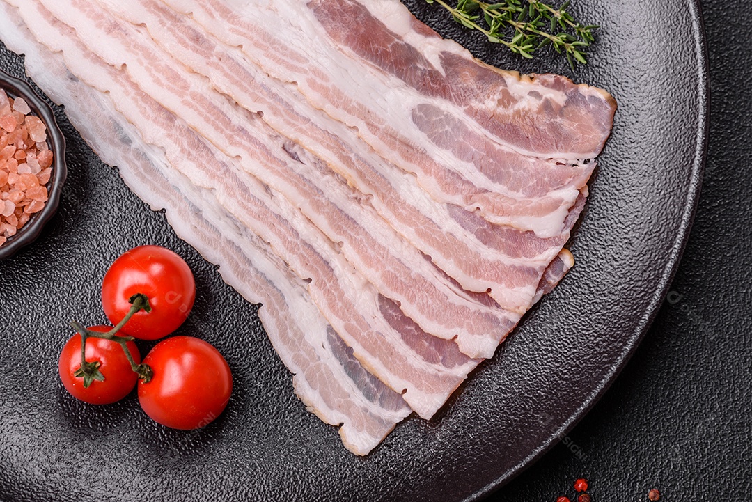 Imagem mostra fatias de bacon cru, acompanhadas de tomates cereja e sal rosa.