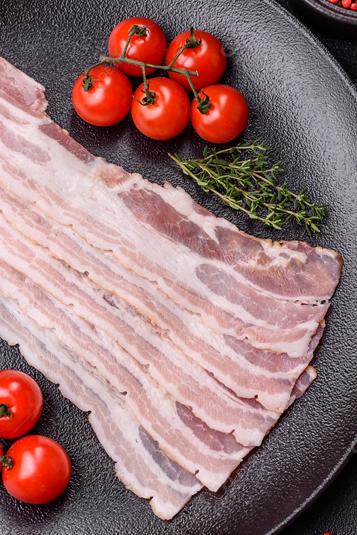 Imagem mostra fatias de bacon cru, acompanhadas de tomates cereja e sal rosa.