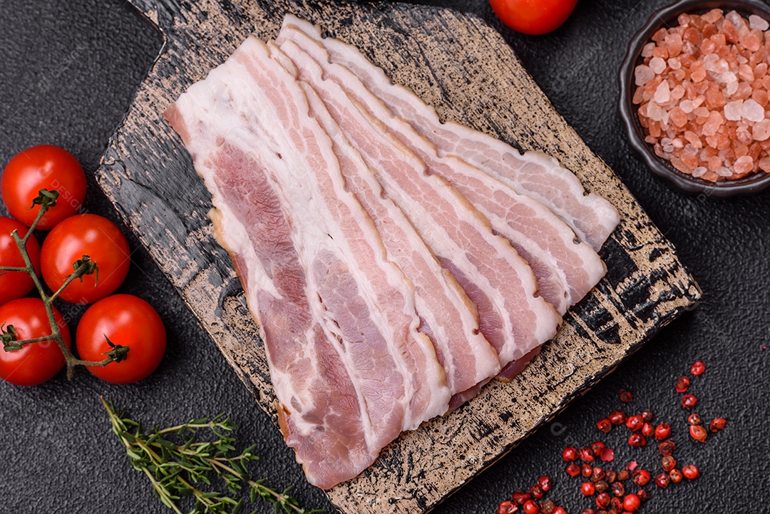 Imagem mostra fatias de bacon cru, acompanhadas de tomates cereja e sal rosa.