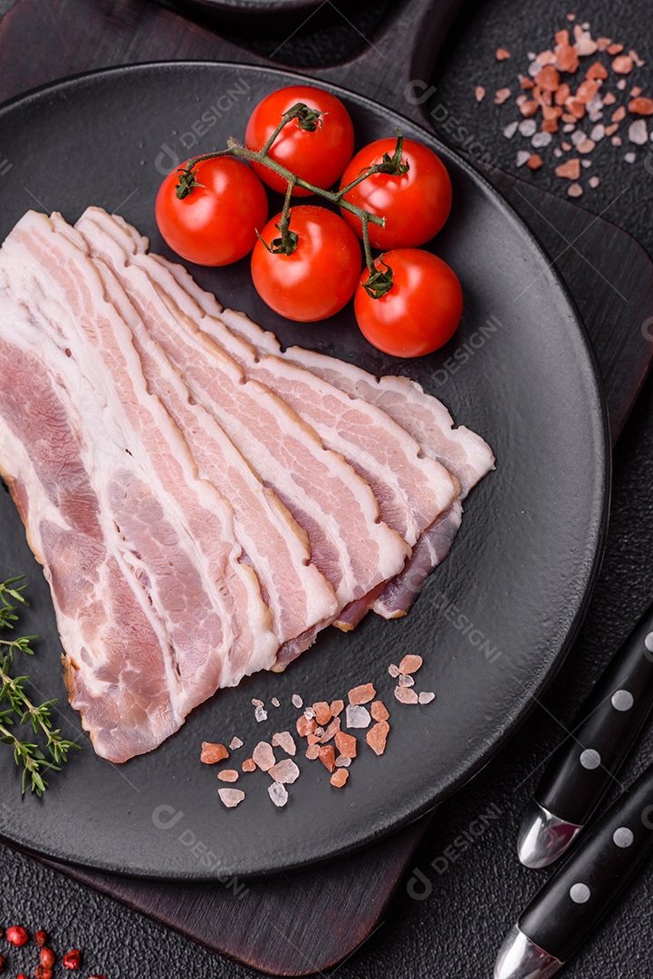 Imagem mostra fatias de bacon cru, acompanhadas de tomates cereja e sal rosa.