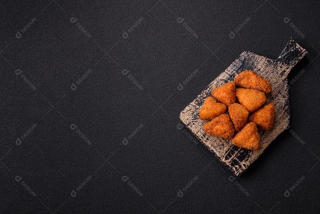 Imagem mostra nuggets de frango com molho e alguns grãos de pimenta rosa