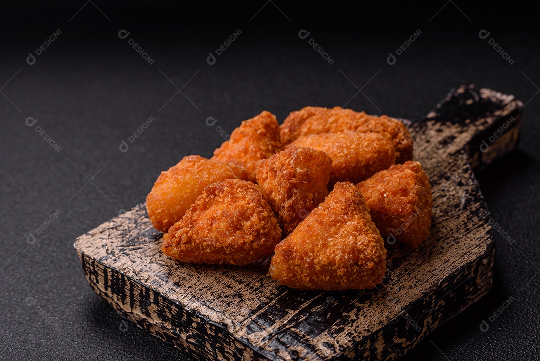 Imagem mostra nuggets de frango com molho e alguns grãos de pimenta rosa