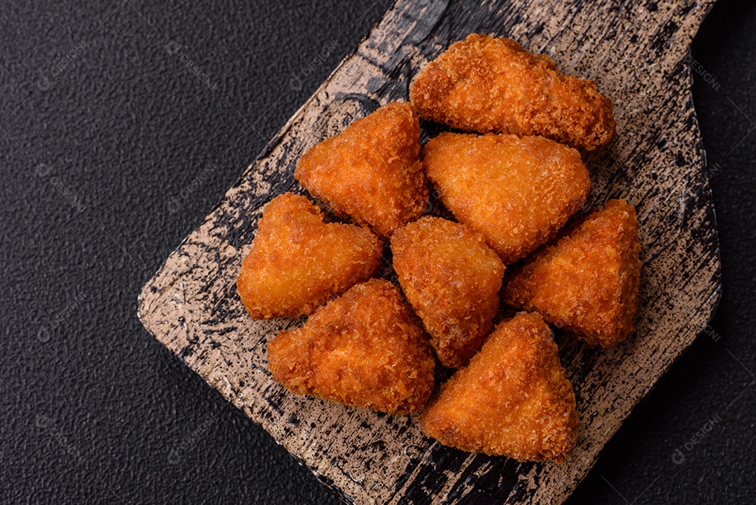 Imagem mostra nuggets de frango com molho e alguns grãos de pimenta rosa