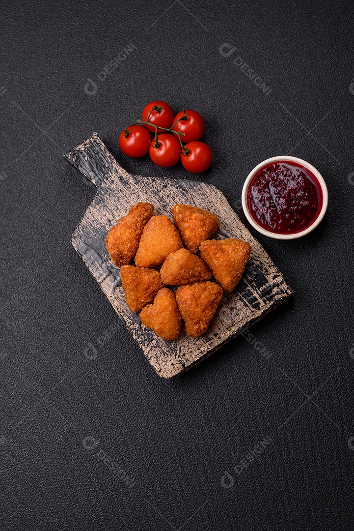 Imagem mostra nuggets de frango com molho e alguns grãos de pimenta rosa