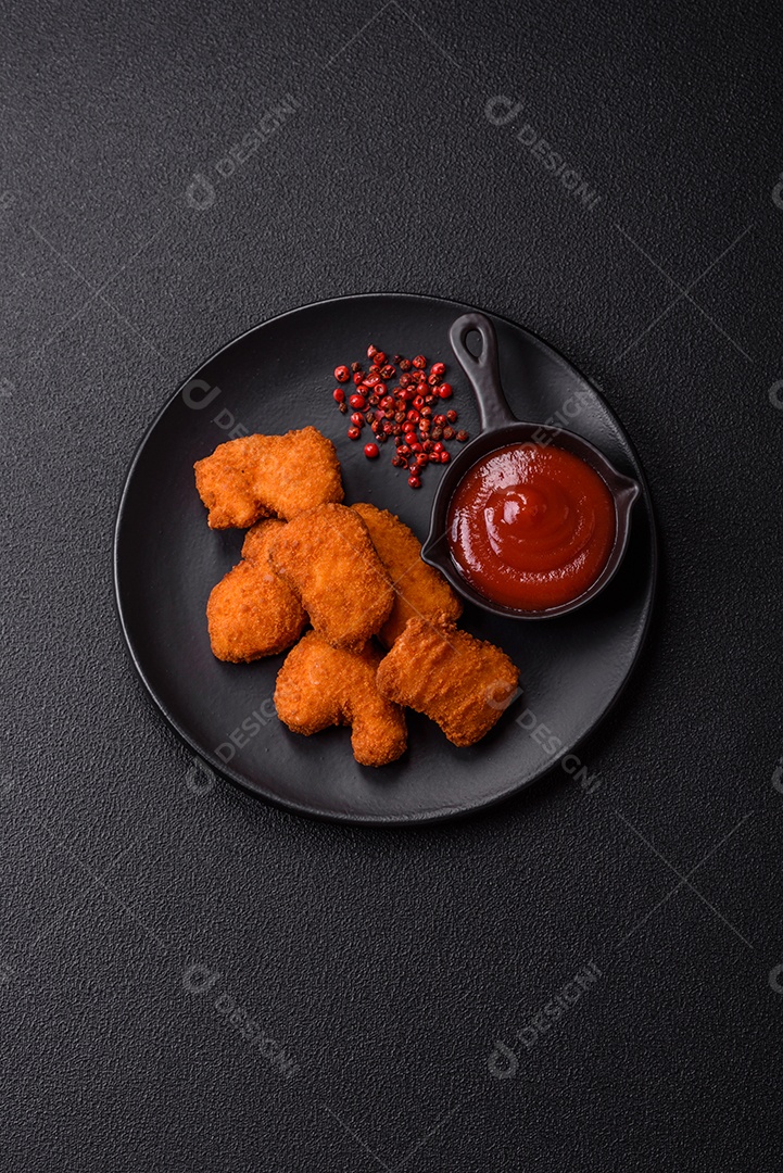 Imagem mostra nuggets de frango com molho e alguns grãos de pimenta rosa