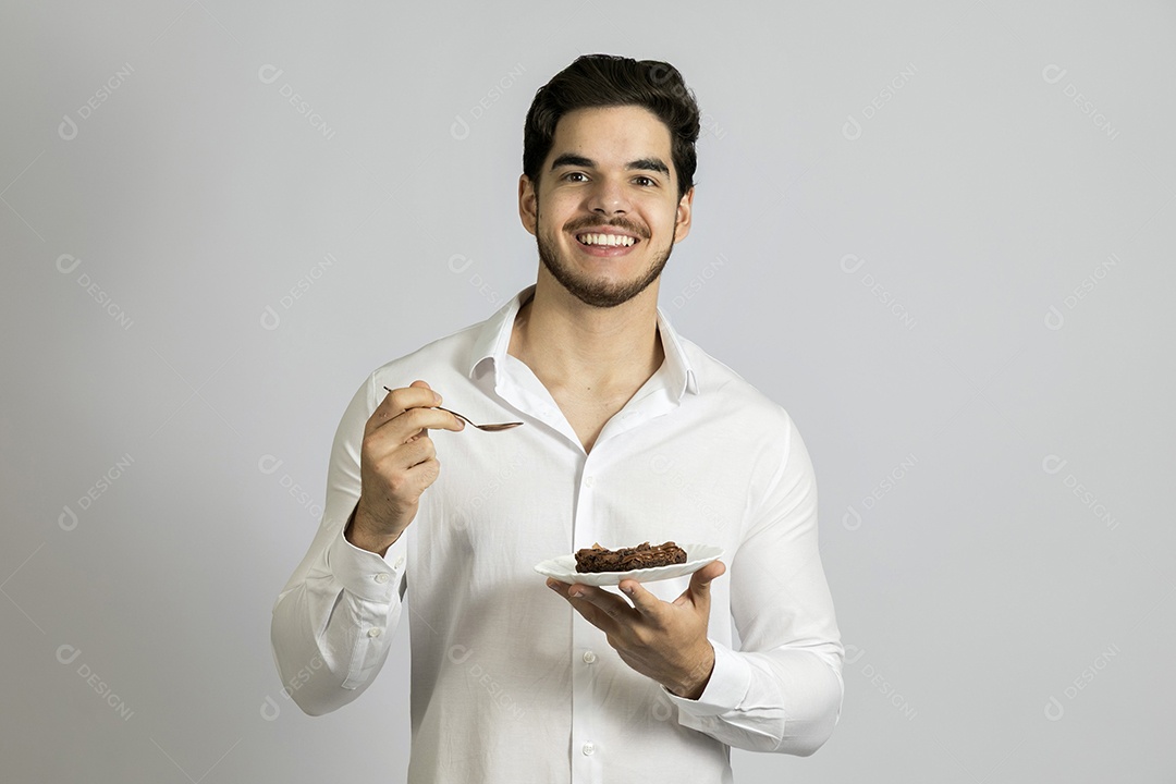 Homem jovem bonito comendo bolo sobre fundo isolado branco