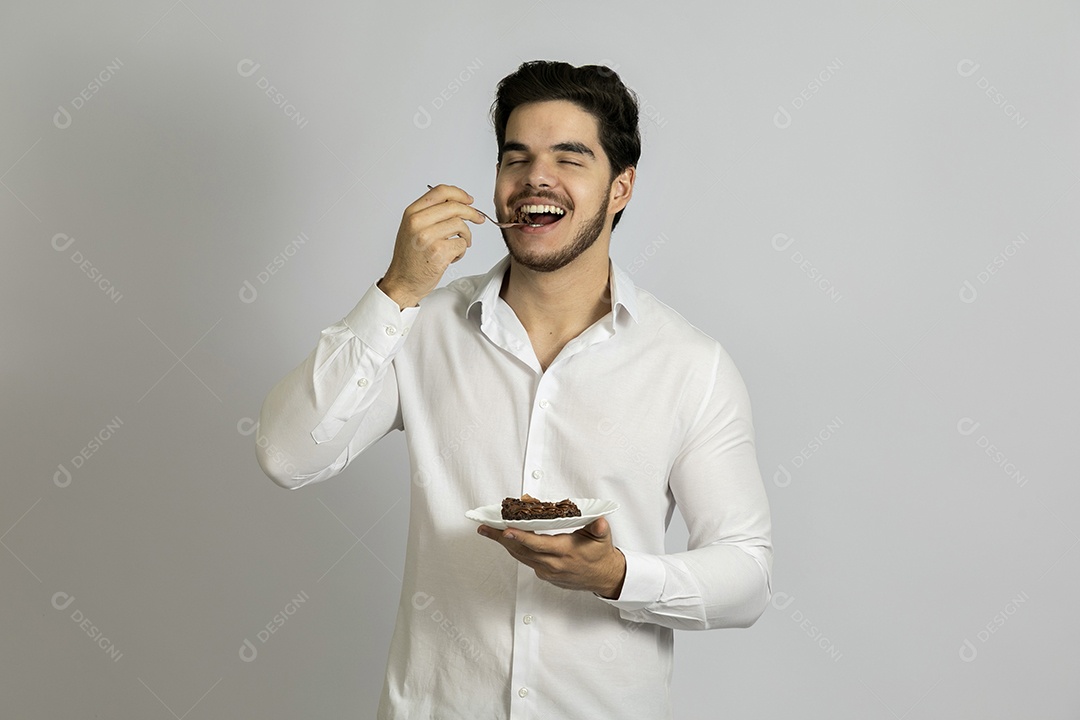 Homem jovem bonito comendo bolo sobre fundo isolado branco