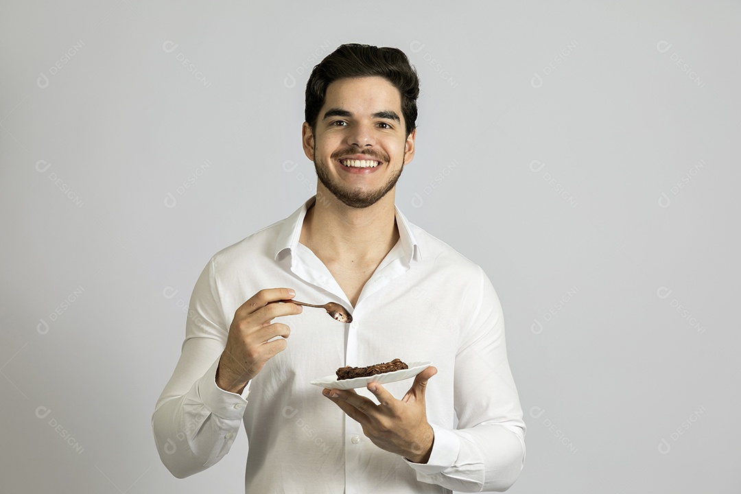 Homem jovem bonito comendo bolo sobre fundo isolado branco