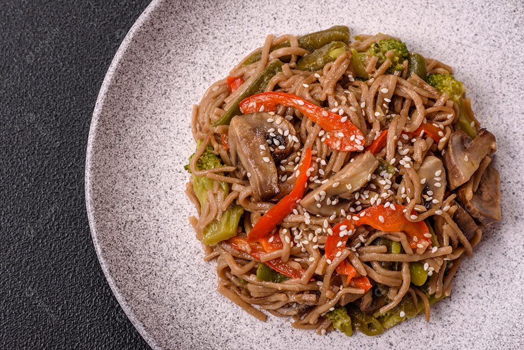 Imagem mostra um prato de noodles asiáticos, possivelmente um tipo de macarrão como Soba ou Udon, servido em uma tigela branca