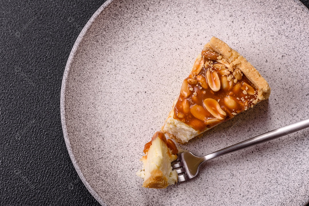 A imagem mostra uma fatia de cheesecake, possivelmente com uma cobertura de caramelo e nozes.
