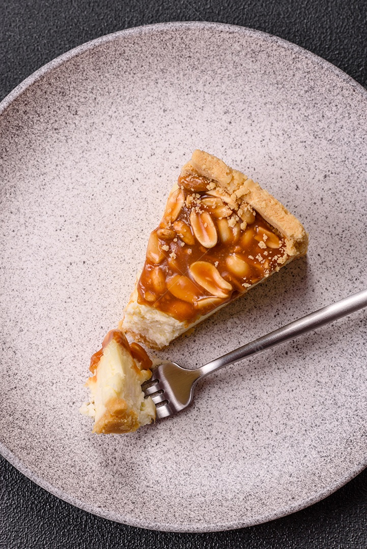 A imagem mostra uma fatia de cheesecake, possivelmente com uma cobertura de caramelo e nozes.