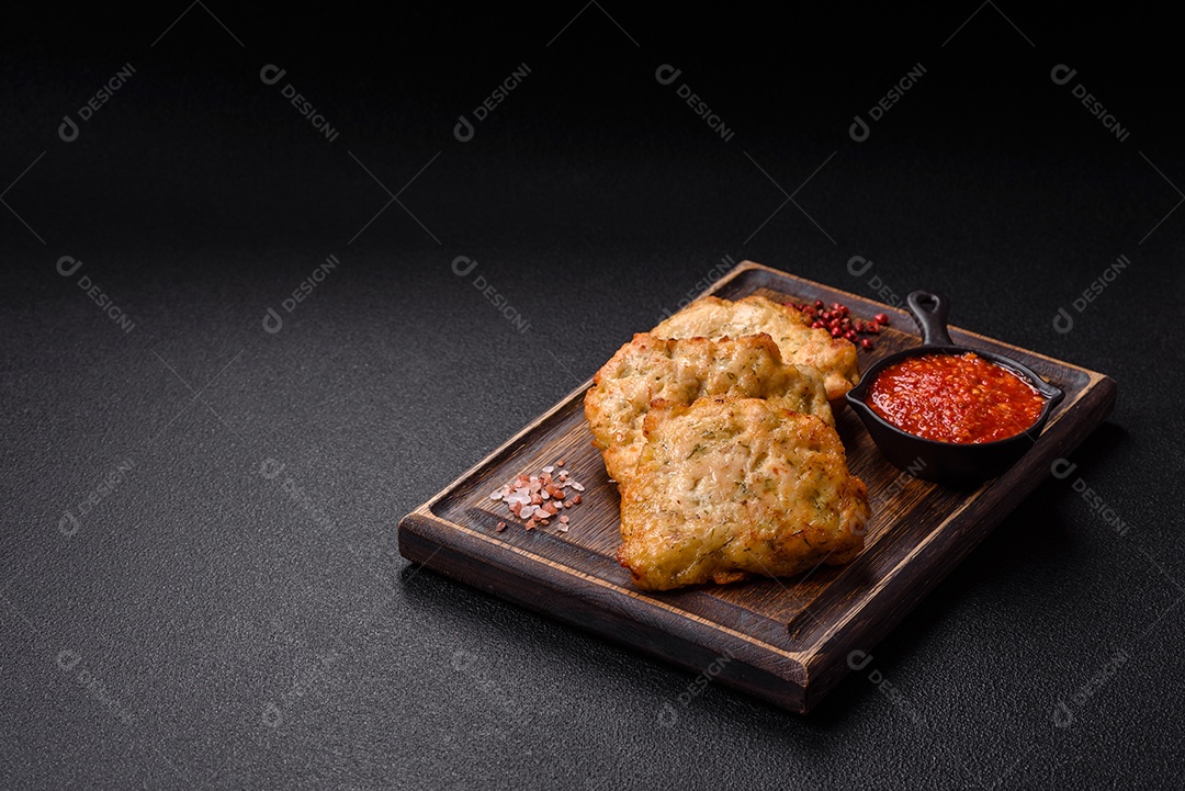 A imagem mostra pedaços de frango frito servidos em uma tábua de madeira com temperos e molho.
