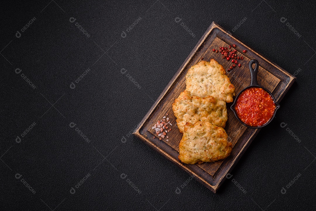 A imagem mostra pedaços de frango frito servidos em uma tábua de madeira com temperos e molho.