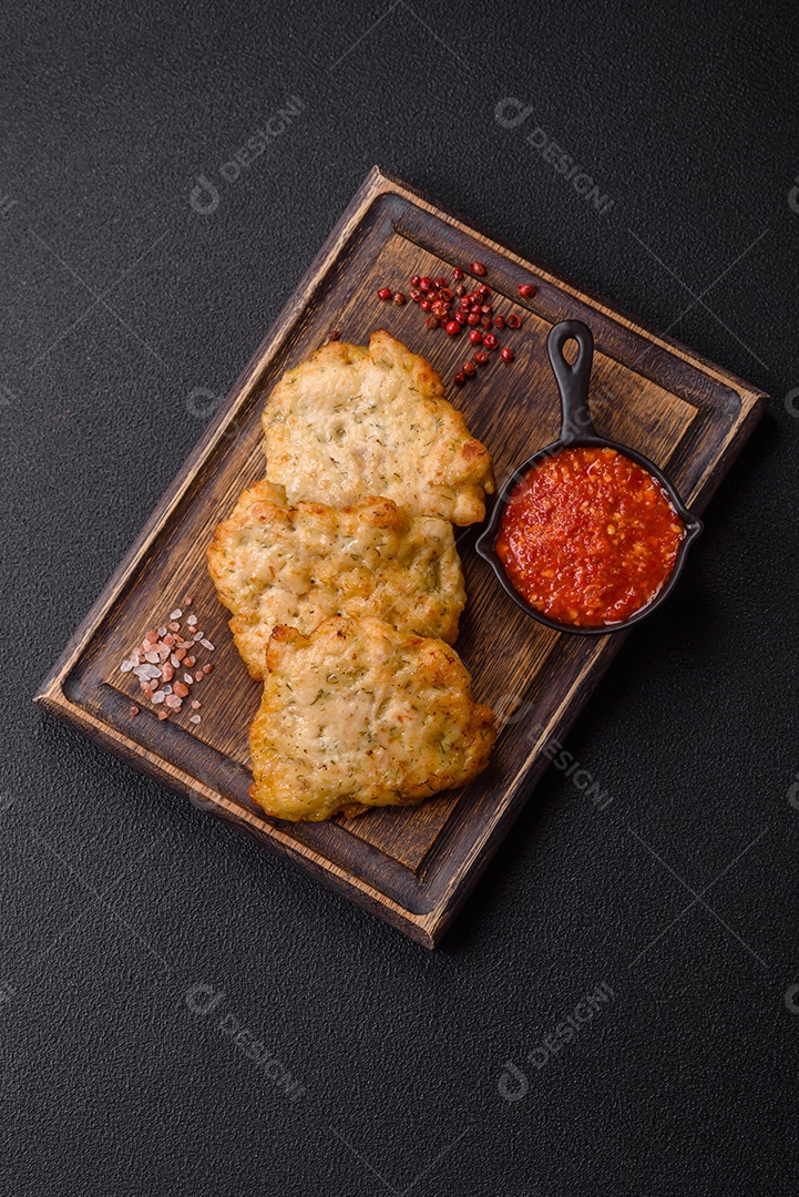 A imagem mostra pedaços de frango frito servidos em uma tábua de madeira com temperos e molho.