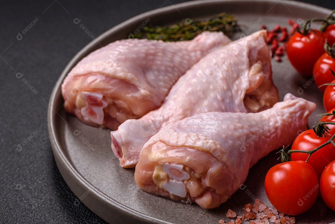 A imagem mostra coxas de frango cruas em um prato, acompanhadas de tomates cereja e ervas frescas.
