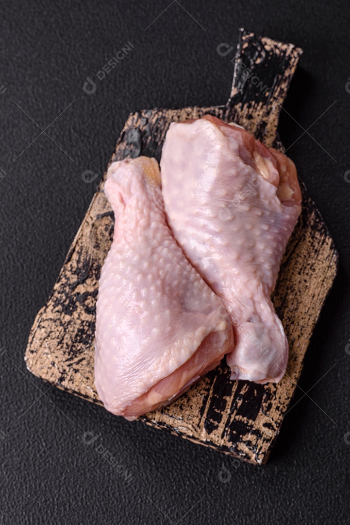 A imagem mostra coxas de frango cruas em um prato, acompanhadas de tomates cereja e ervas frescas.