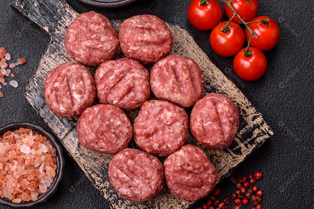 A imagem mostra almôndegas de carne cruas, prontas para serem cozidas, acompanhadas de tomates e pimenta rosa.