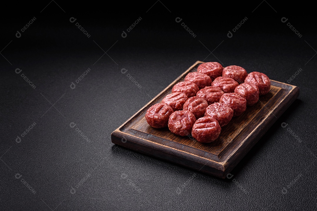 A imagem mostra almôndegas de carne cruas, prontas para serem cozidas, acompanhadas de tomates e pimenta rosa.