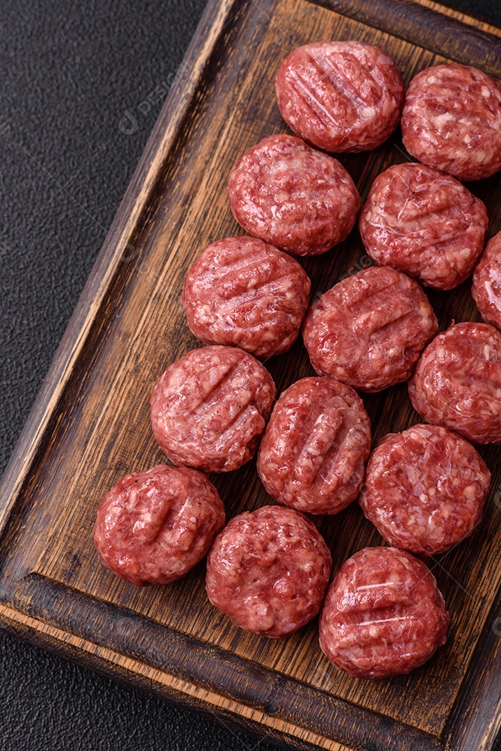 A imagem mostra almôndegas de carne cruas, prontas para serem cozidas, acompanhadas de tomates e pimenta rosa.