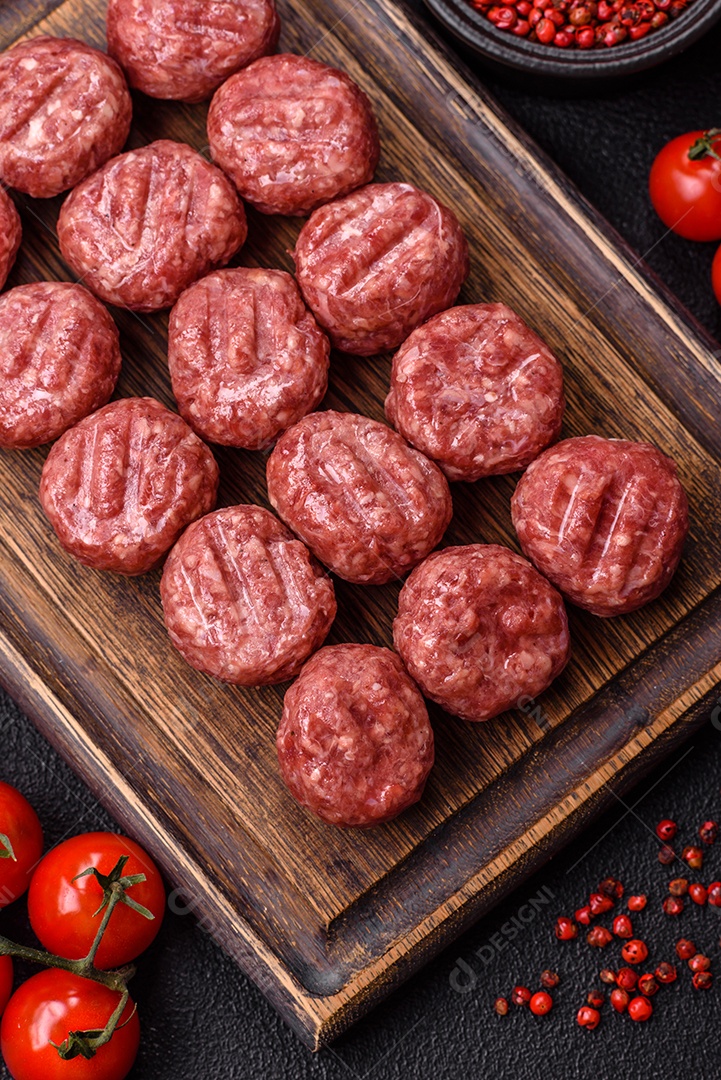 A imagem mostra almôndegas de carne cruas, prontas para serem cozidas, acompanhadas de tomates e pimenta rosa.