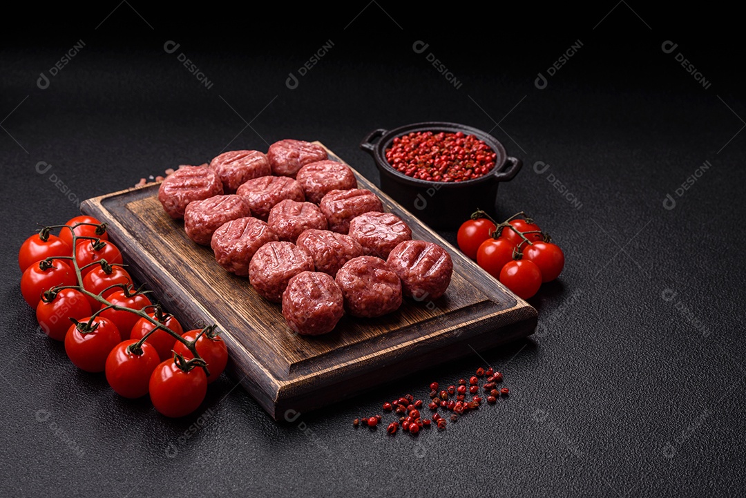 A imagem mostra almôndegas de carne cruas, prontas para serem cozidas, acompanhadas de tomates e pimenta rosa.