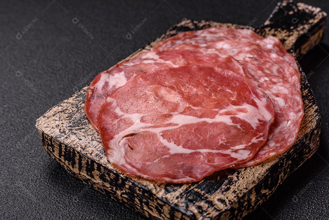 A imagem mostra um prato de embutidos, com destaque para fatias de salame e presunto cru, acompanhados de tomates-cereja e pimenta rosa