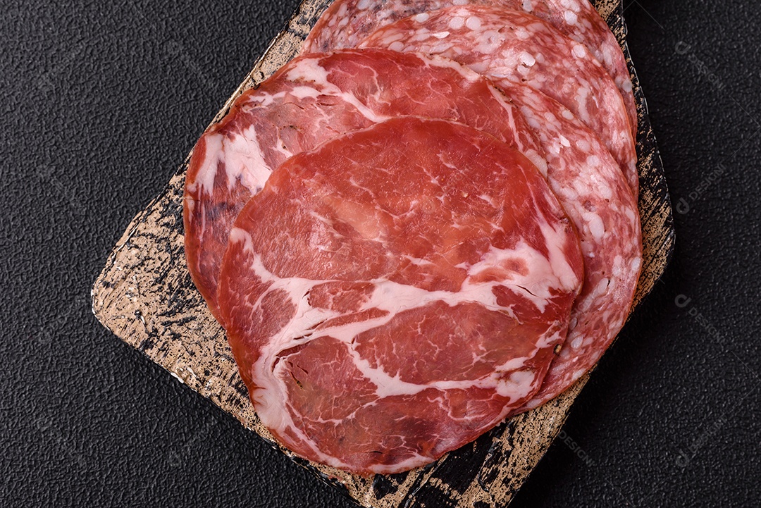 A imagem mostra um prato de embutidos, com destaque para fatias de salame e presunto cru, acompanhados de tomates-cereja e pimenta rosa