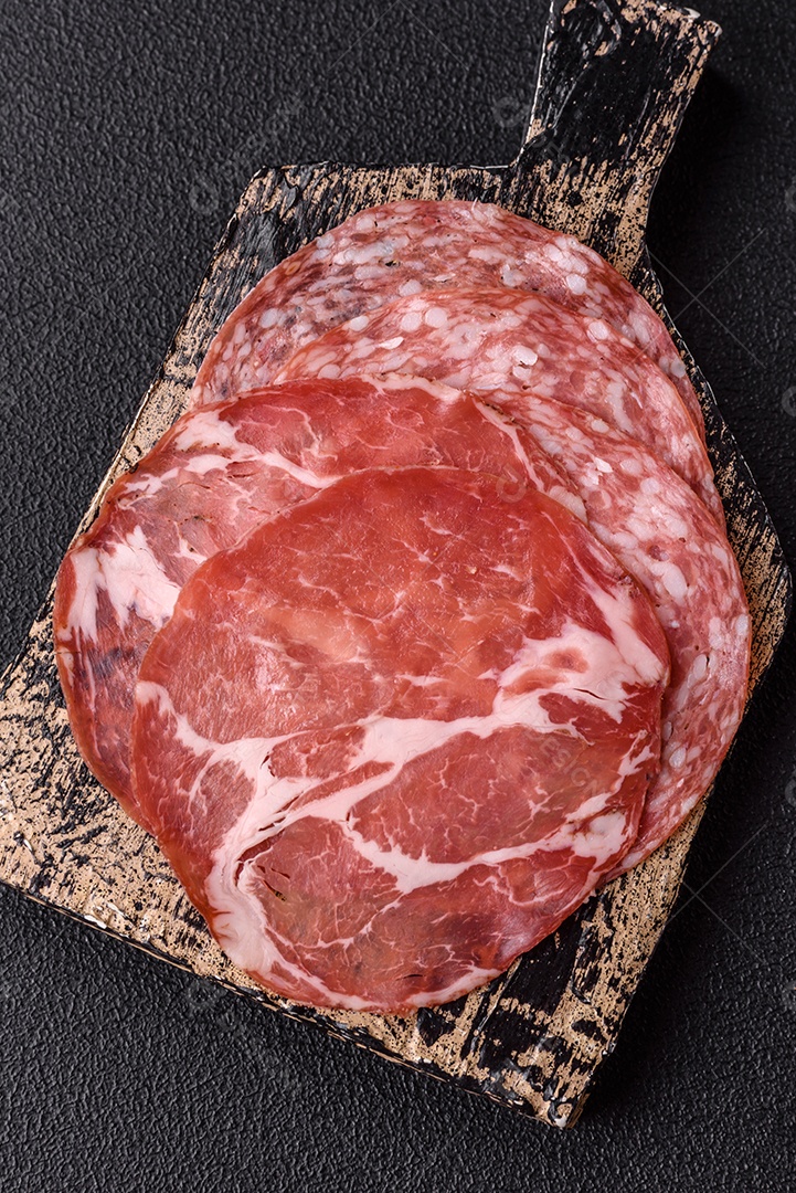 A imagem mostra um prato de embutidos, com destaque para fatias de salame e presunto cru, acompanhados de tomates-cereja e pimenta rosa